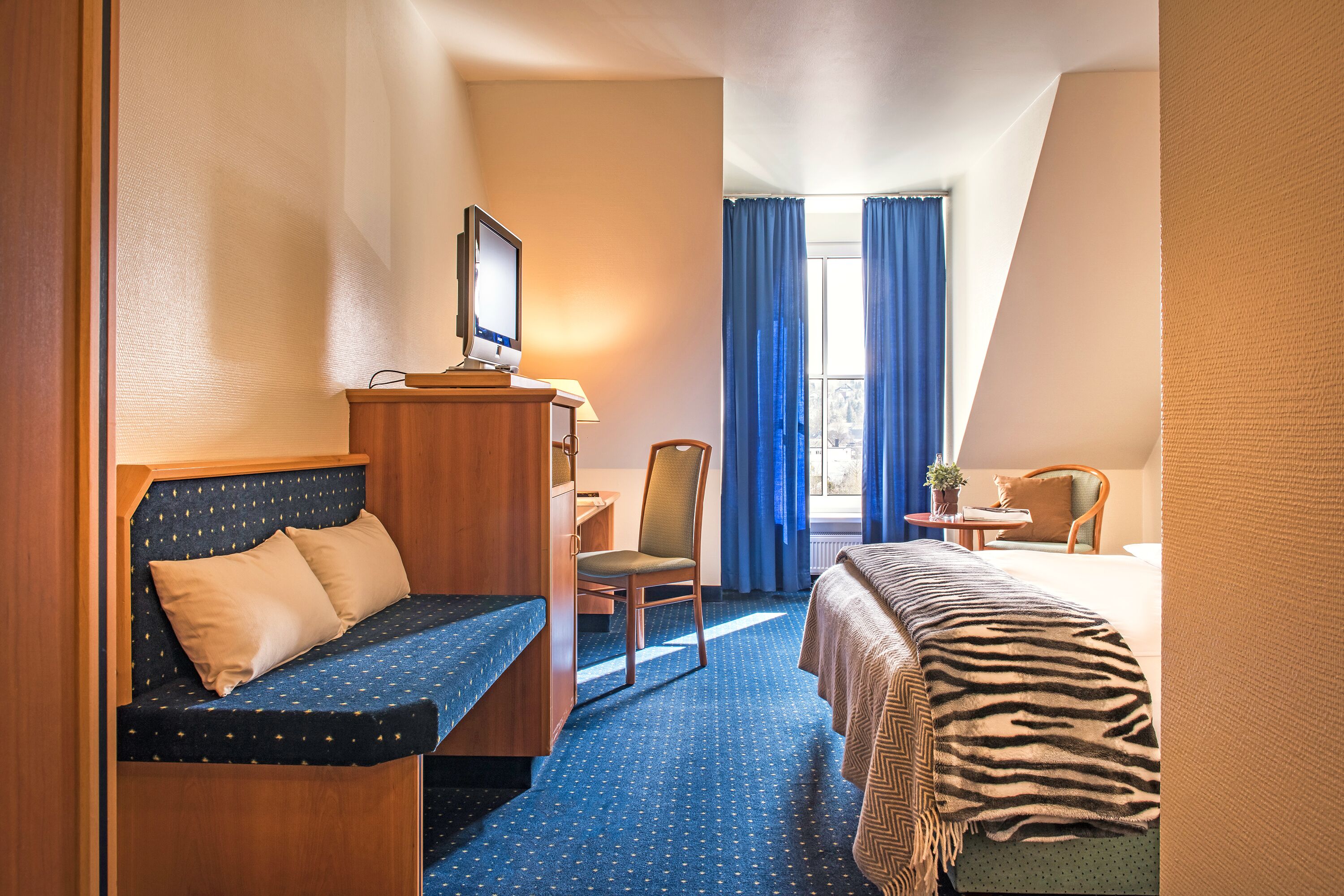 A hotel room with a bed, a desk, a chair, and a small table.