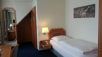 Una habitación de hotel con cama, lámpara de noche, teléfono, espejo, escritorio y un cuadro en la pared.
