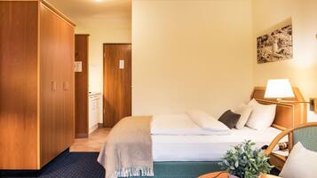 A hotel room with a bed, a bedside table with a lamp, a potted plant, and a wardrobe.