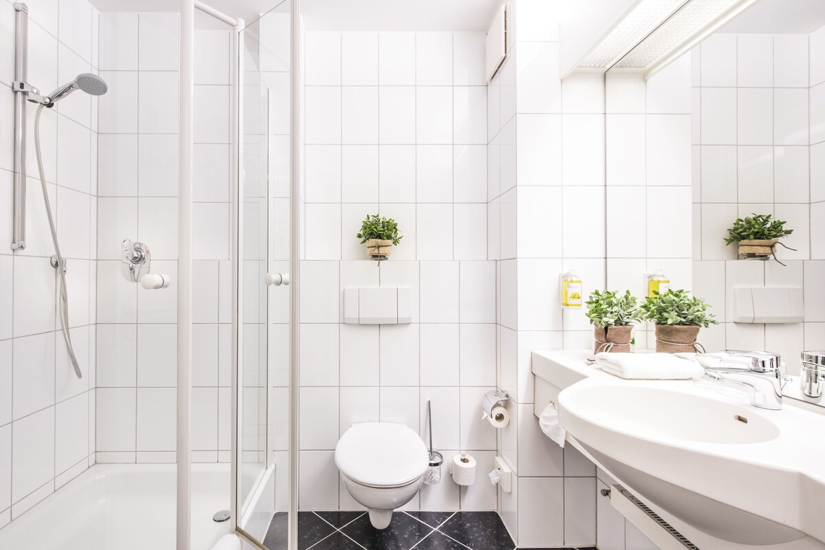 Un baño moderno con ducha de vidrio, inodoro blanco y un lavamanos grande con espejo.