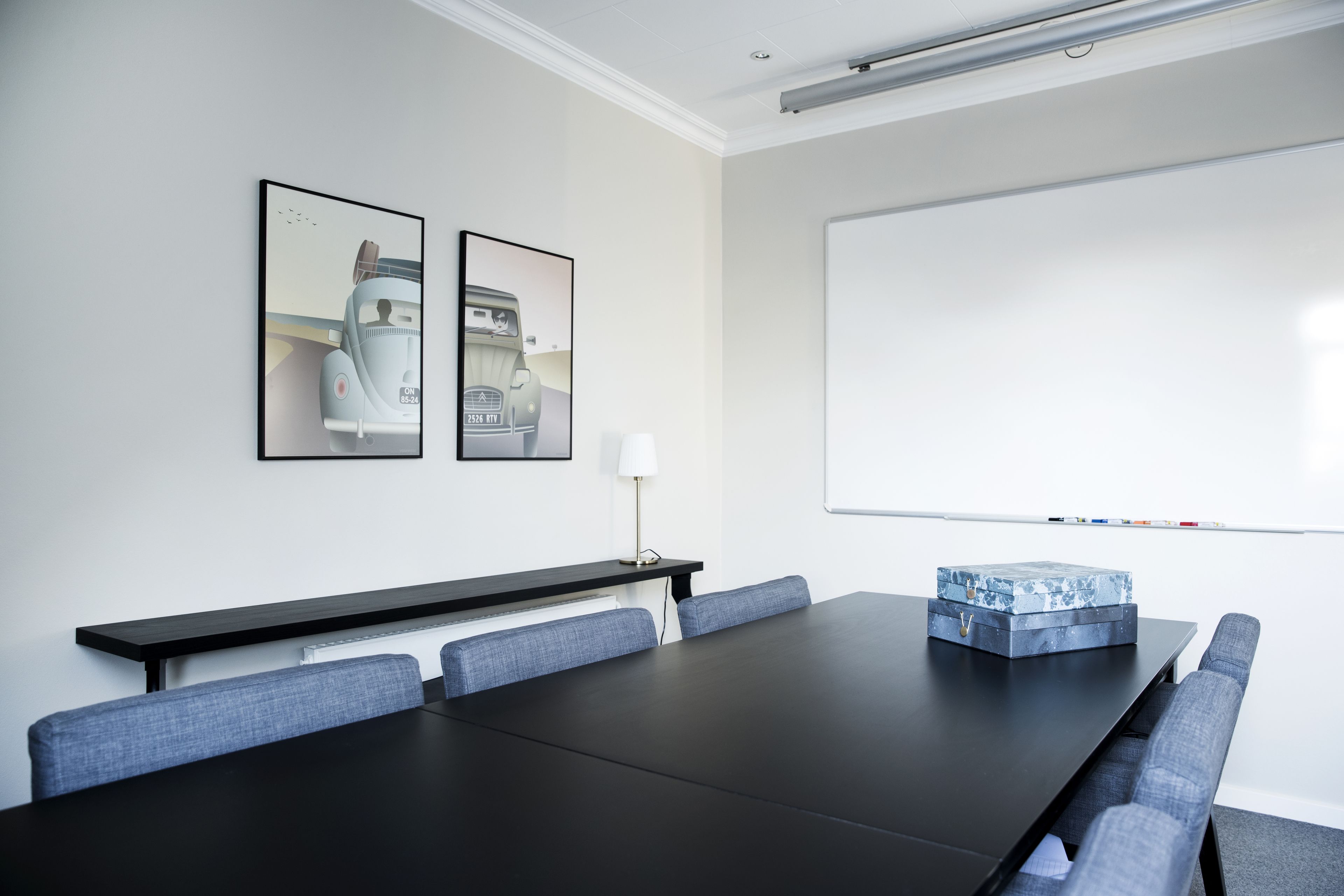 A conference room with a long table, blue upholstered chairs, a whiteboard, and two framed pictures on the wall.