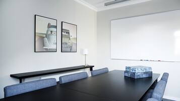 A conference room with a long table, blue upholstered chairs, a whiteboard, and two framed pictures on the wall.