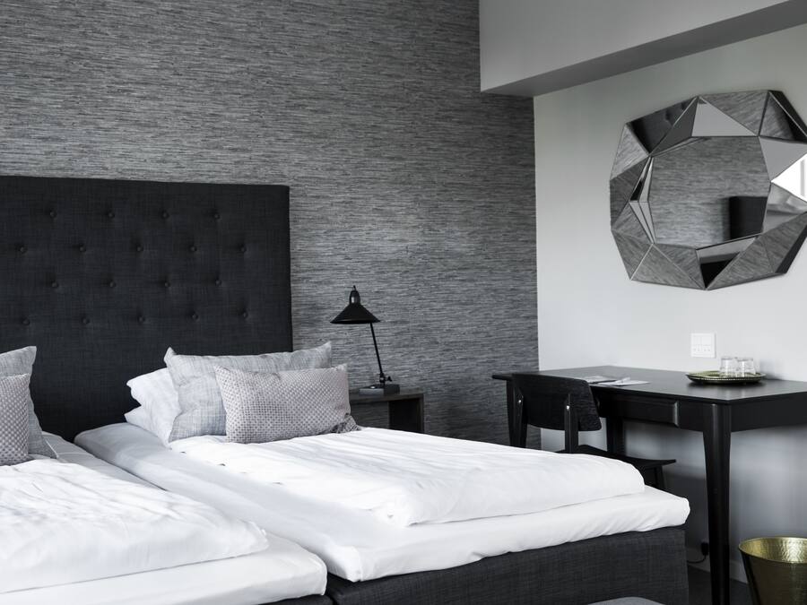 Una habitación de hotel moderna con una cama grande, un escritorio y un espejo geométrico único en la pared.