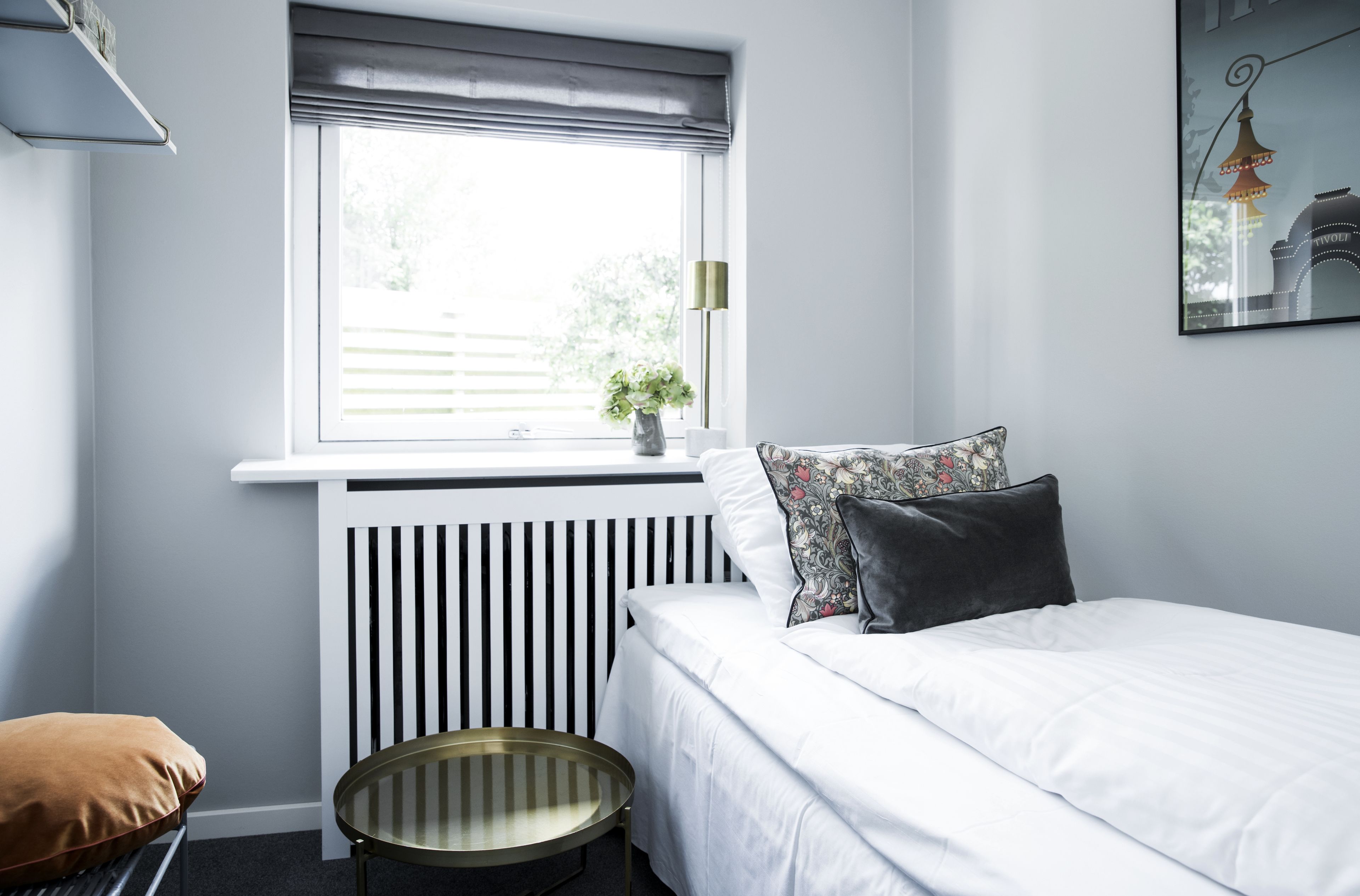 Un dormitorio con cama, radiador, ventana con persianas, mesita de noche y una silla.