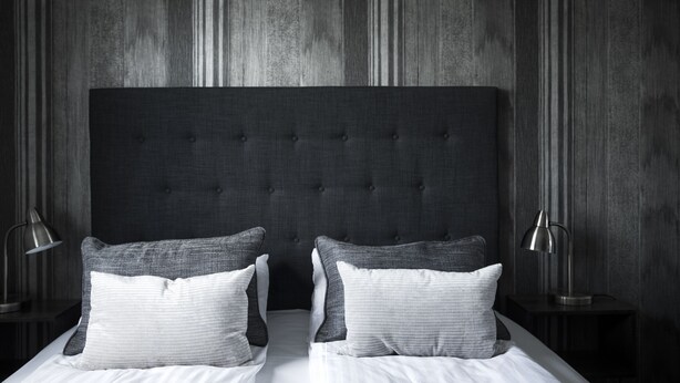 A bedroom with a tufted headboard, two bedside tables with lamps, and a bed with pillows. - Skjalm Hvide Hotel (Slangerup)