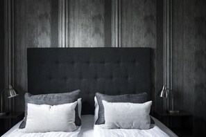 Un dormitorio con cabecera capitonada, dos mesitas de noche con lámparas y una cama con almohadas.