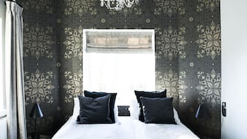 A bedroom with a large bed, dark patterned wallpaper, a chandelier, and a window.