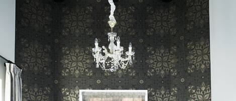Un dormitorio con una cama grande, papel tapiz oscuro con diseño, una araña y una ventana.
