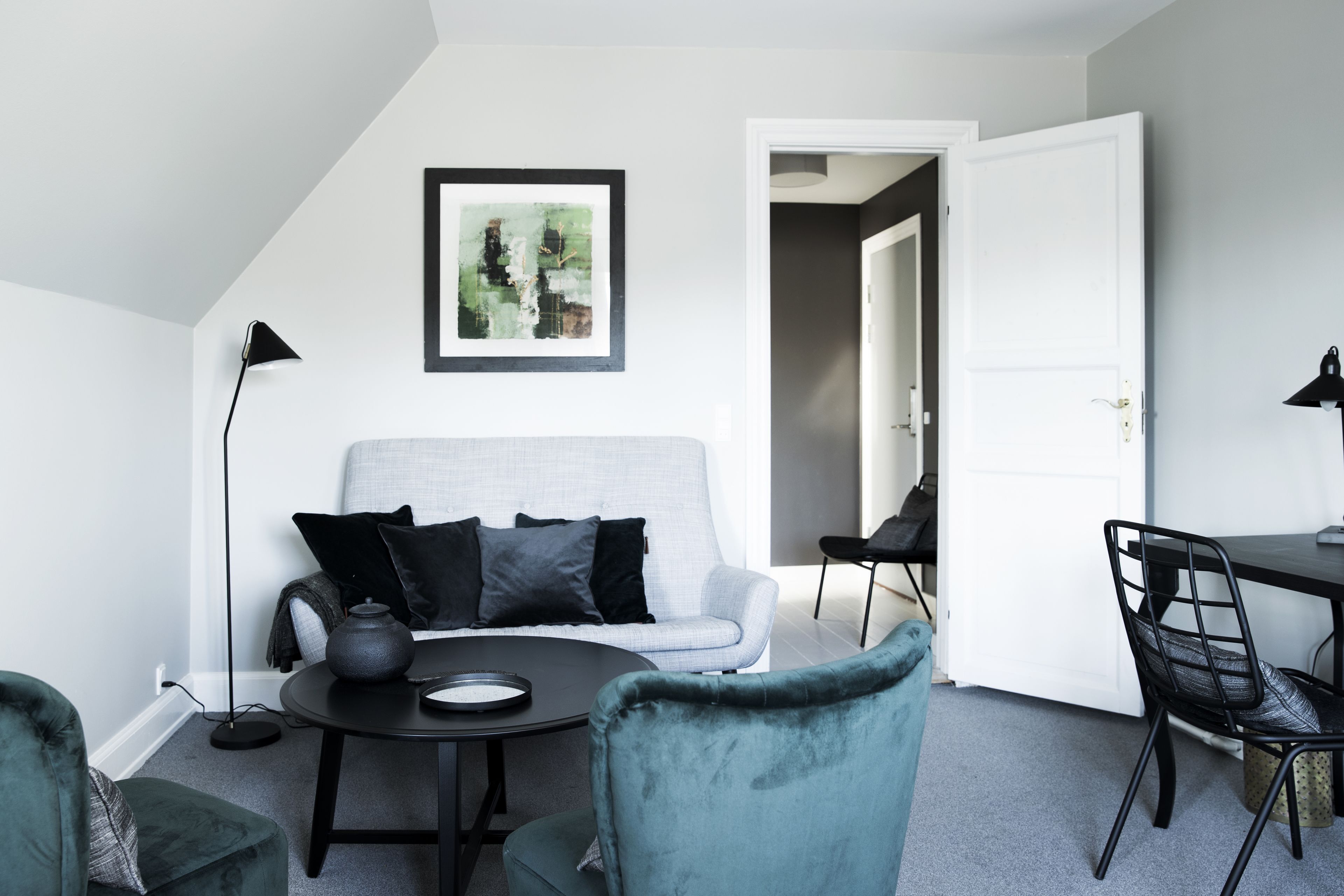 Una sala de estar moderna con un sofá gris, cojines negros, una mesa de centro redonda y un sillón color turquesa.