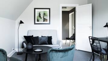 Una sala de estar moderna con un sofá gris, cojines negros, una mesa de centro redonda y un sillón color turquesa.