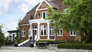 A brick building with a white balcony, a staircase leading to the entrance, and outdoor seating area with tables and chairs. - Skjalm Hvide Hotel (Slangerup)