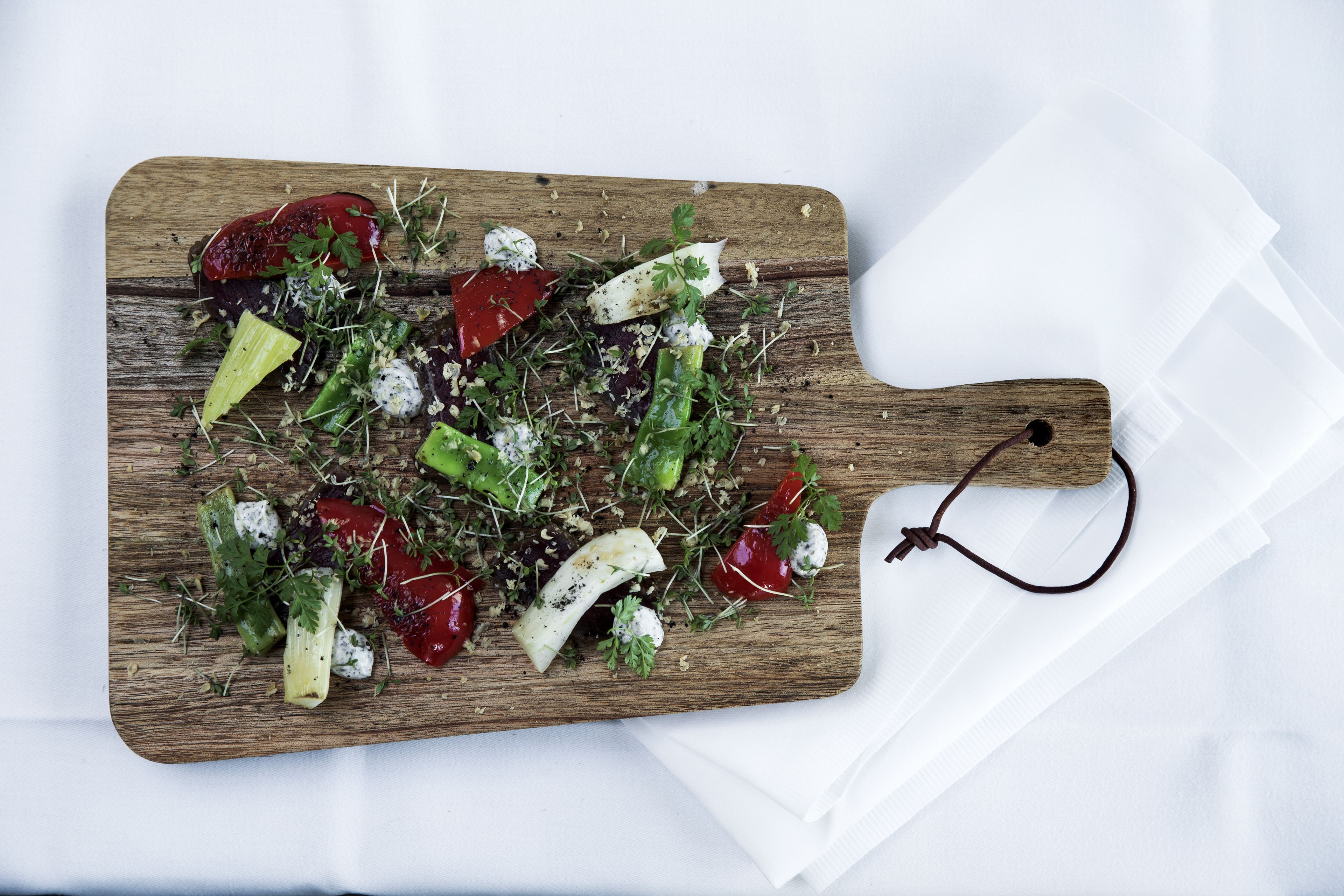 A wooden cutting board with a variety of vegetables and cheese on a white surface.