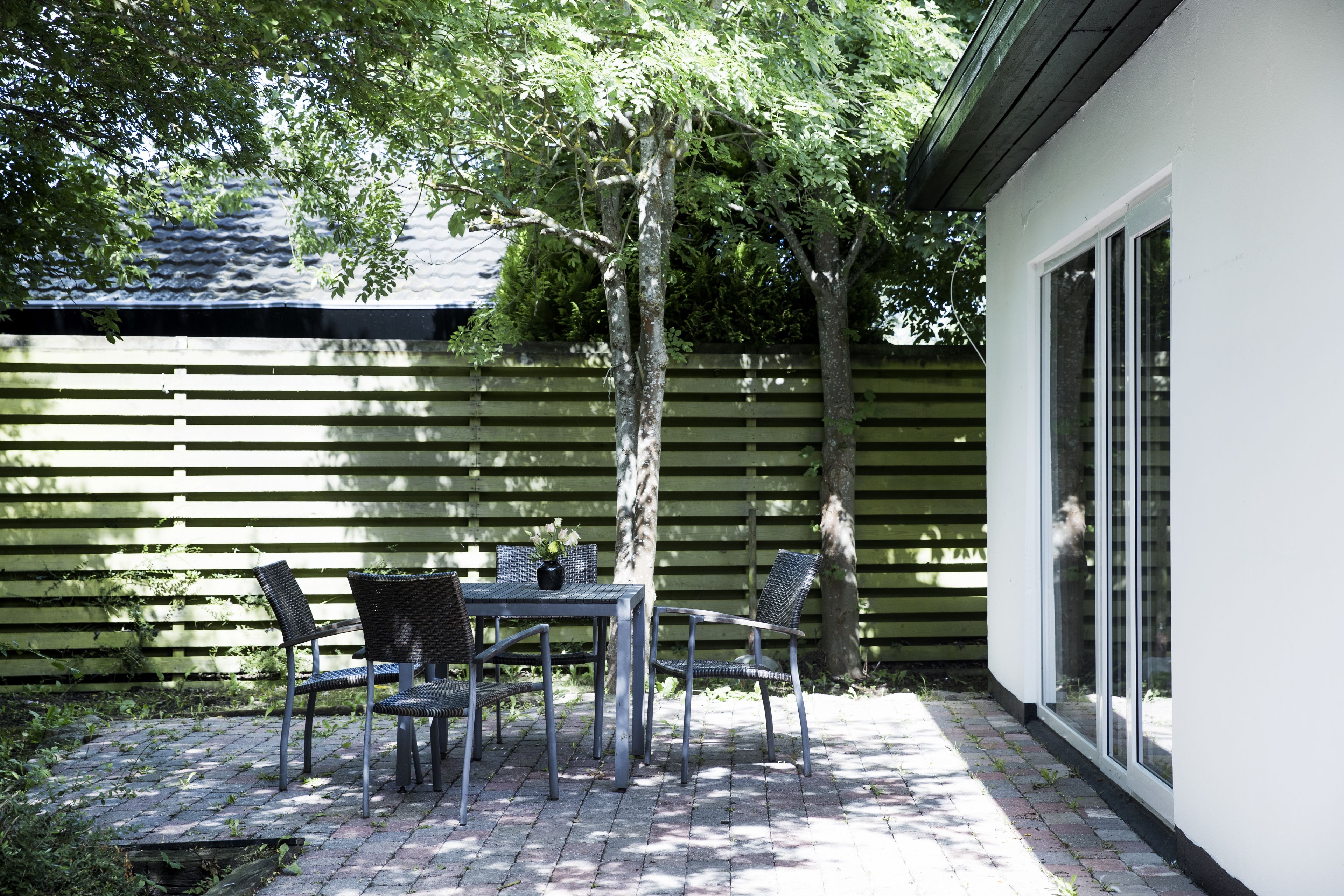 Un patio con una mesa y sillas, una cerca de madera y un edificio con ventanas amplias.