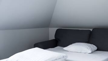 A modern, minimalist bedroom with a dark-colored sofa and a neatly made bed with white bedding.