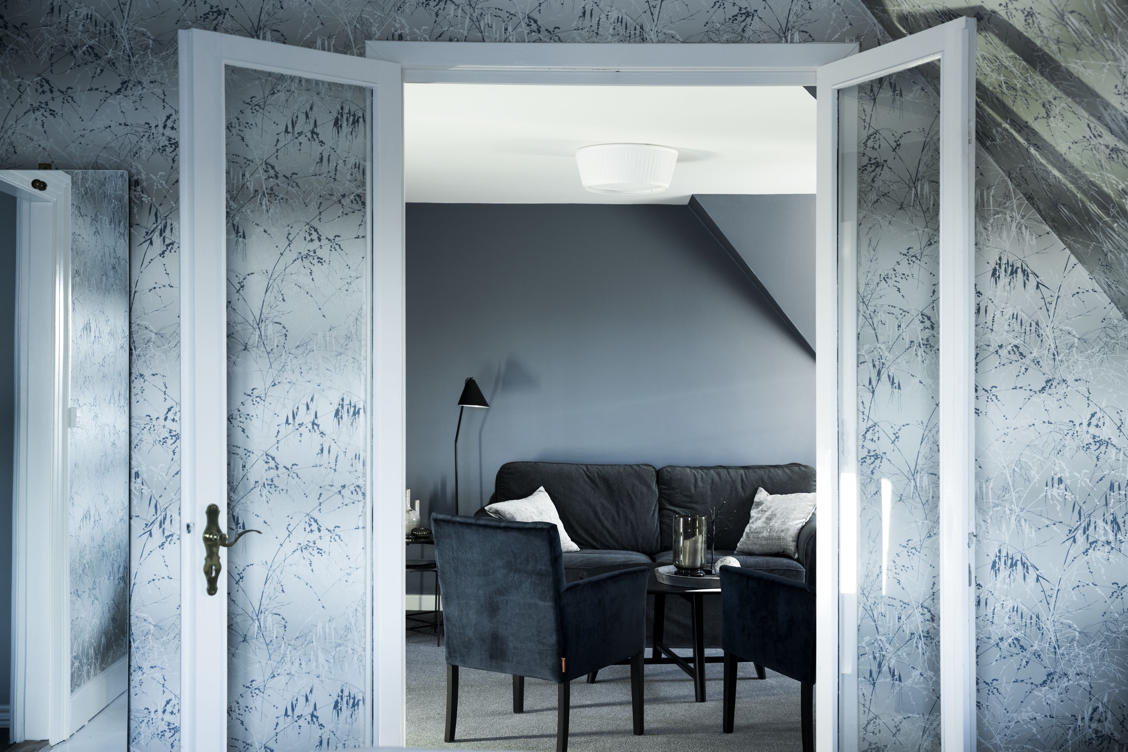 A modern living room with a dark blue sofa, two armchairs, and a small table with a vase.