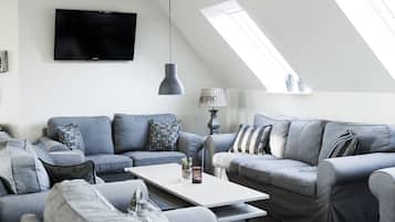 Una sala de estar moderna con un televisor de pantalla plana, sofás grises, una mesa de centro blanca y una lámpara.