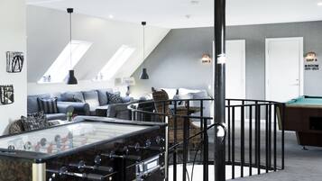 A modern living room with a foosball table, a pool table, and a comfortable seating area with a sofa and armchairs.