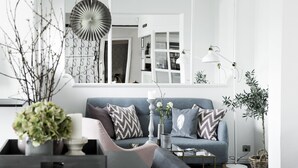 A modern living room with a grey sofa, patterned cushions, a white vase with flowers, a floor lamp, and a potted plant. - Skjalm Hvide Hotel (Slangerup)