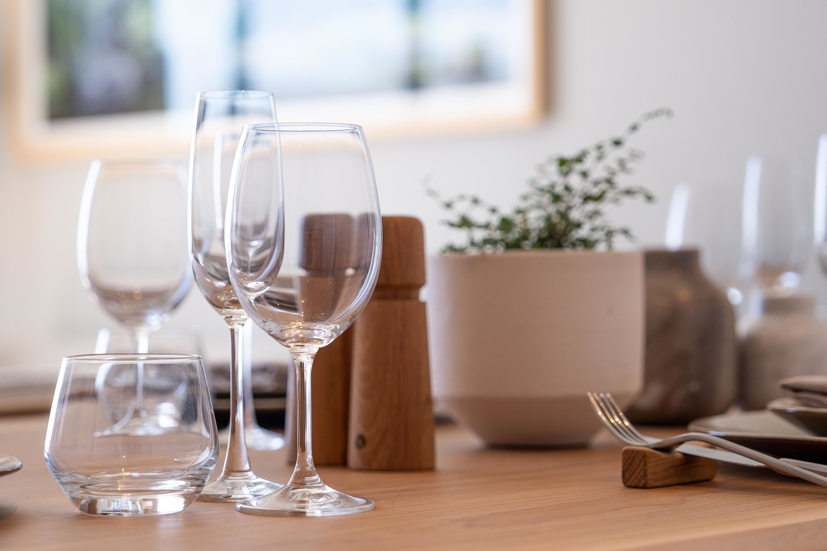 A dining table with wine glasses, a wooden block, and a salt shaker.