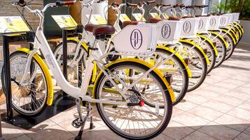 Una hilera de bicicletas con cestas, cada una con un logotipo, estacionadas en un espacio al aire libre con piso de baldosas.
