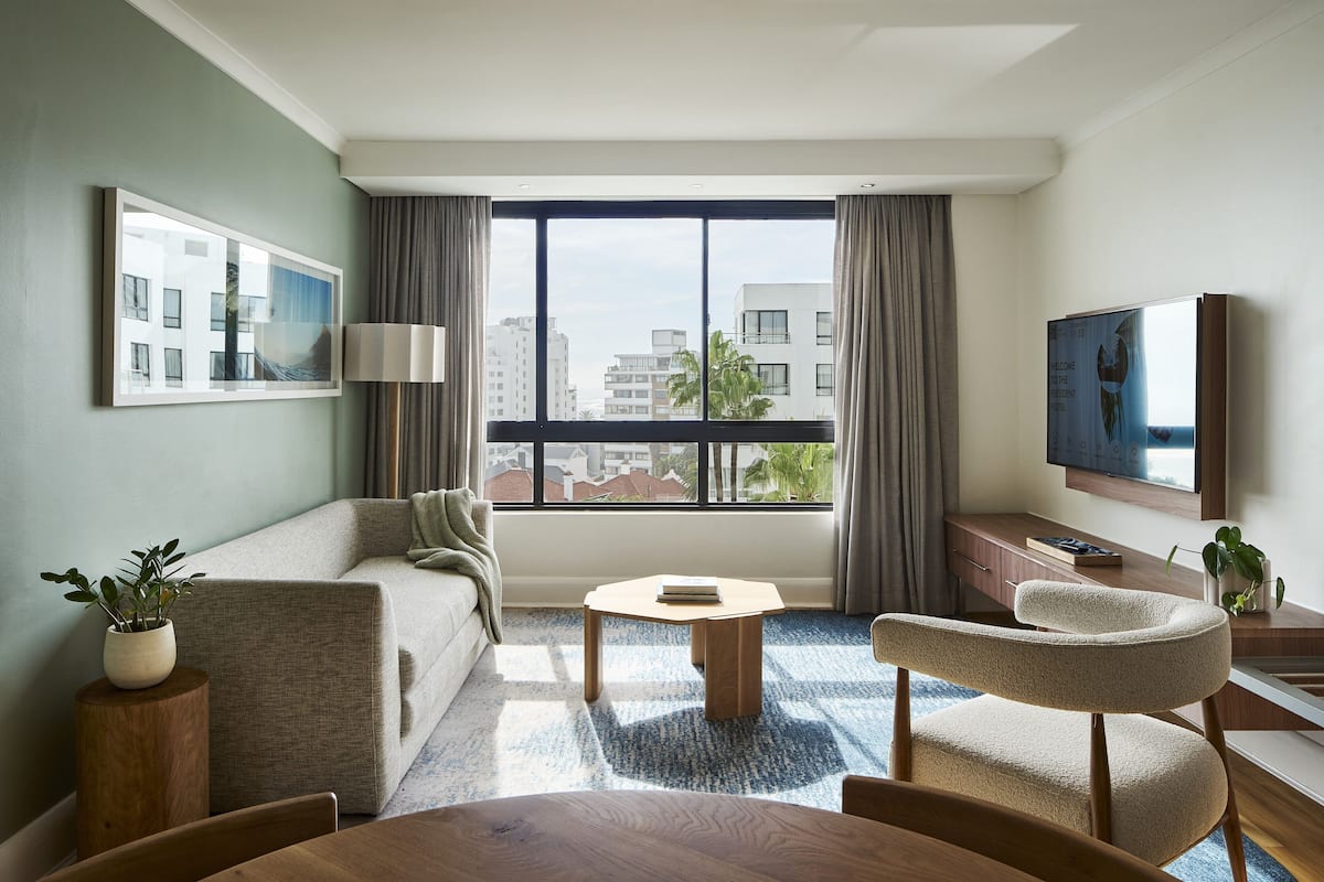 Ein modernes Hotelzimmer mit großem Fenster, einer Couch, einem Couchtisch, einem Fernseher und einem Schreibtisch.