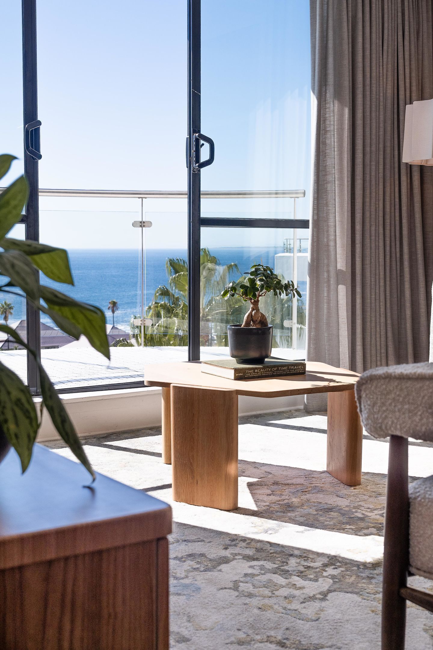 A room with a large window, a wooden table, a potted plant, and a chair.