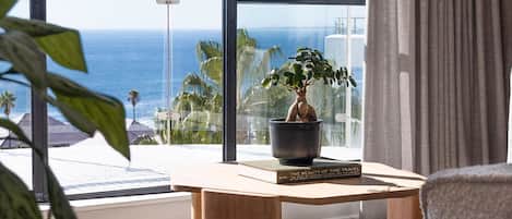 A room with a large window, a wooden table, a potted plant, and a chair.
