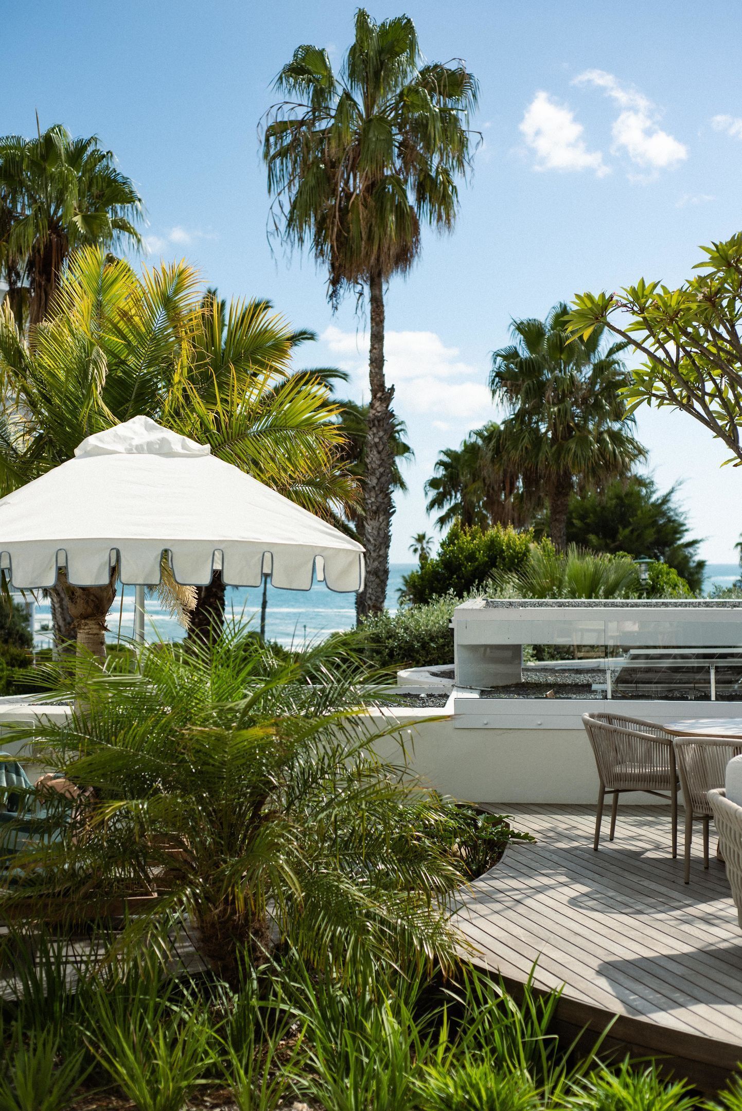 Une terrasse en bois avec des meubles d’extérieur, un parasol blanc et des palmiers.
