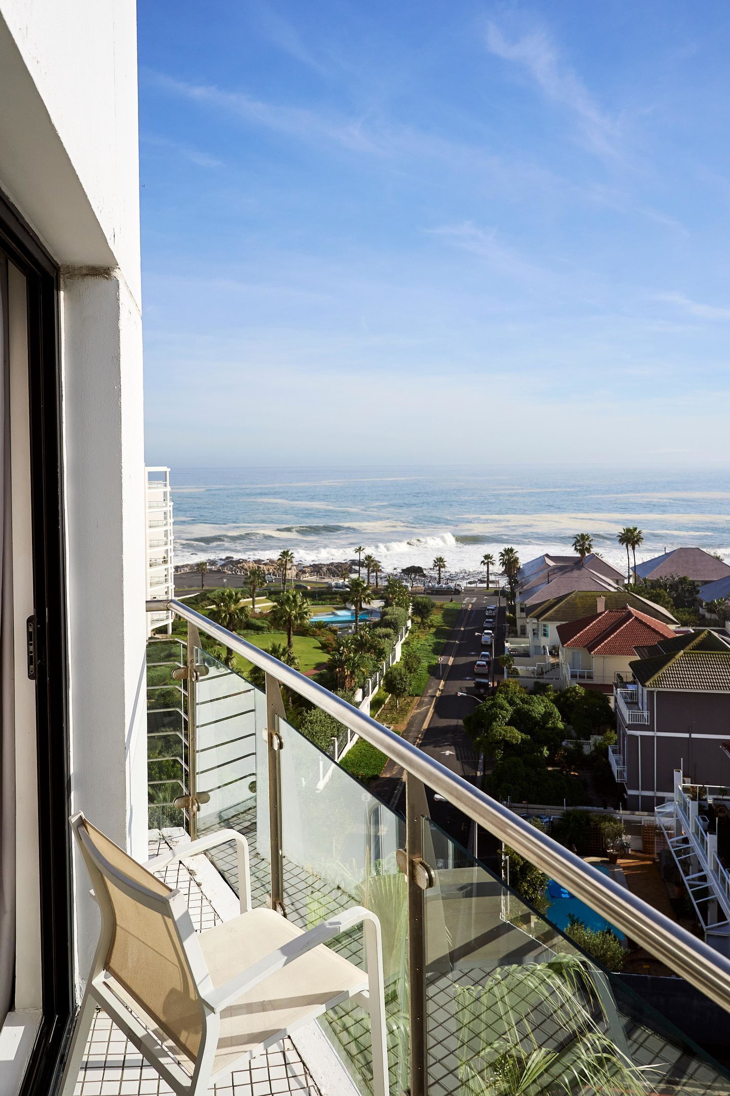 A balcony with a view of the ocean, a pool, and residential buildings.