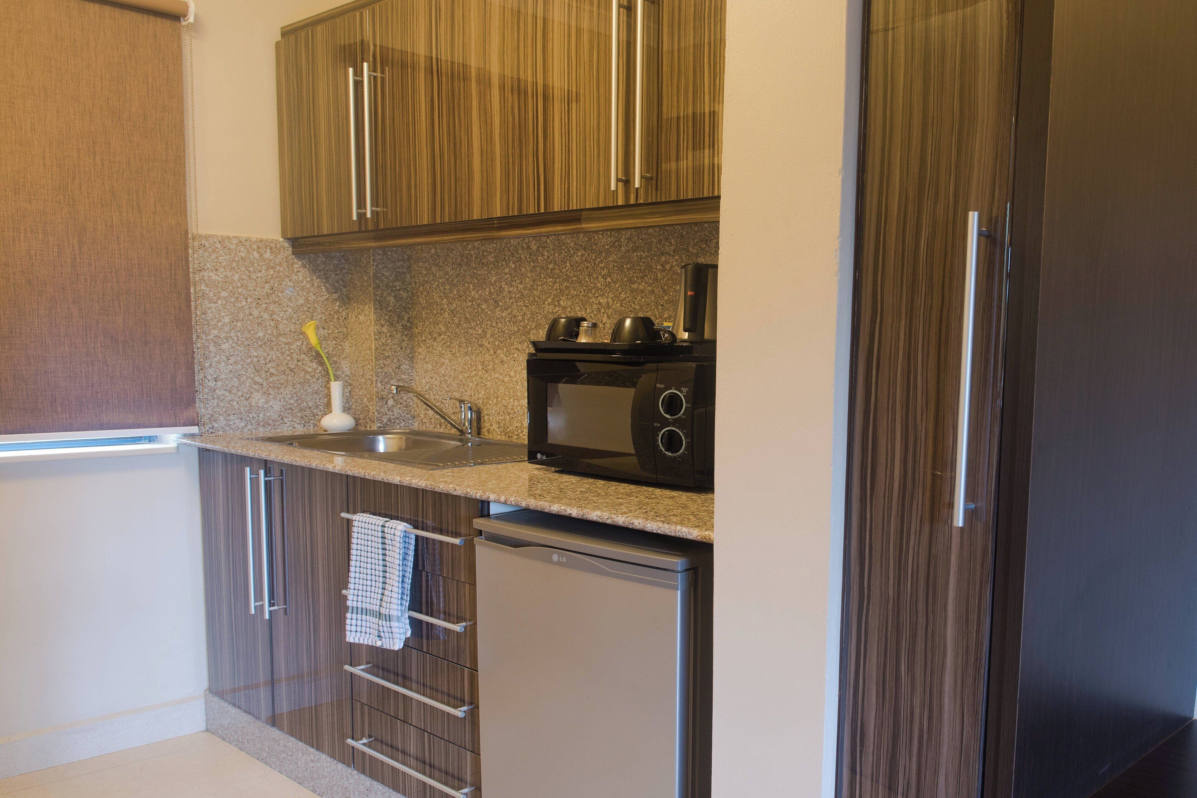 Una cocina moderna con armarios de madera, encimera de granito, microondas integrado y refrigerador de acero inoxidable.