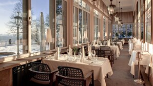 En restaurang med bord uppdukade för middag, stora fönster och hängande lampor.