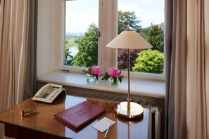 A wooden desk with a telephone, a book, a lamp, and a vase with flowers by a window. - Hotel Schloss Eckberg (Dresden)