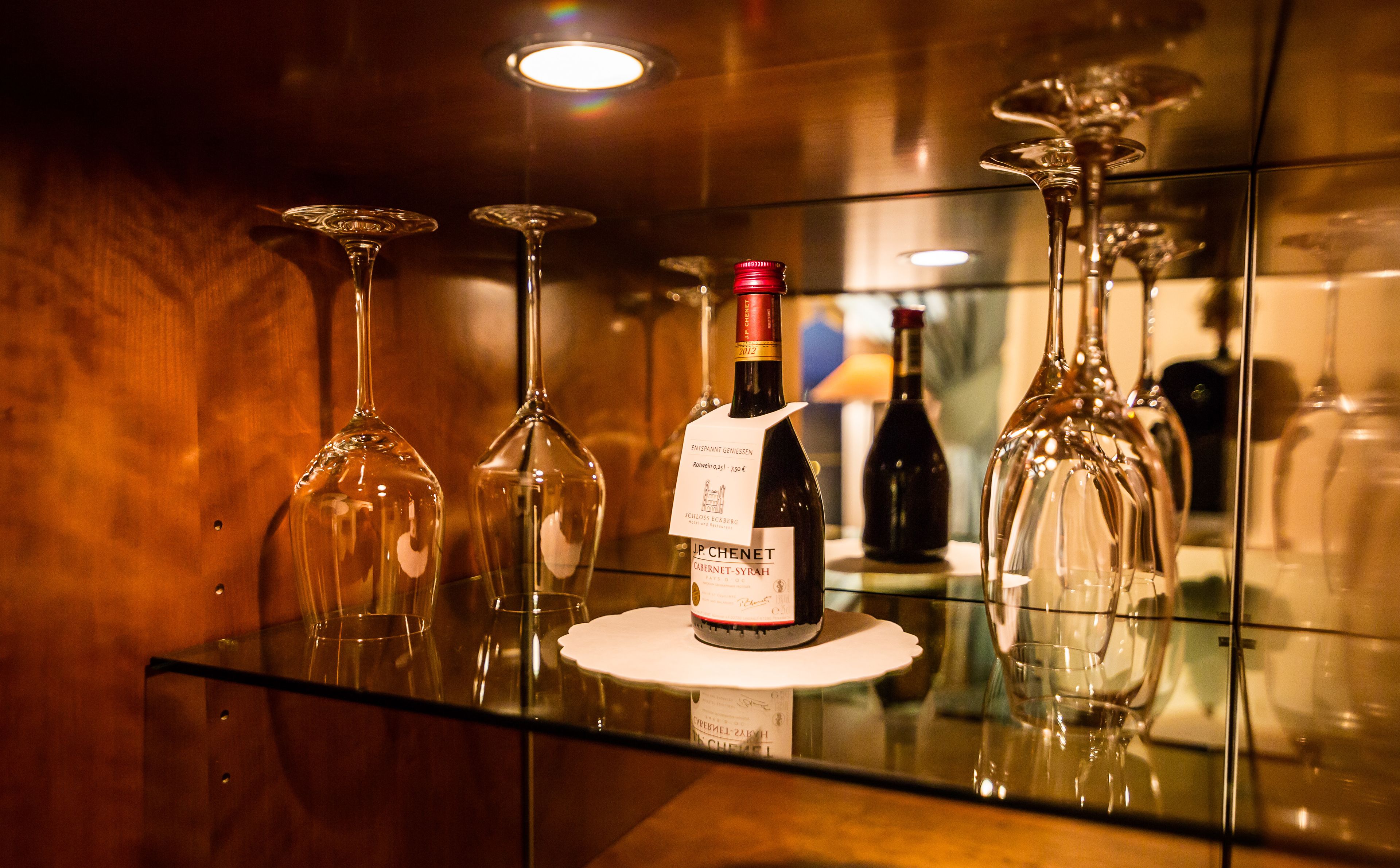 Una botella de vino con etiqueta sobre una mesa de vidrio rodeada de copas vacías.