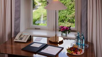 Escritorio de habitación de hotel con teléfono, lámpara, un jarrón con flores y una bandeja de frutas.