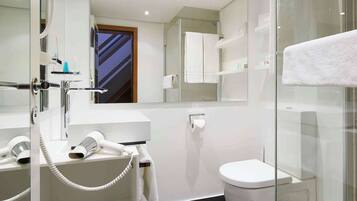 A modern bathroom with a glass shower enclosure, a white sink with a telephone, and a toilet.
