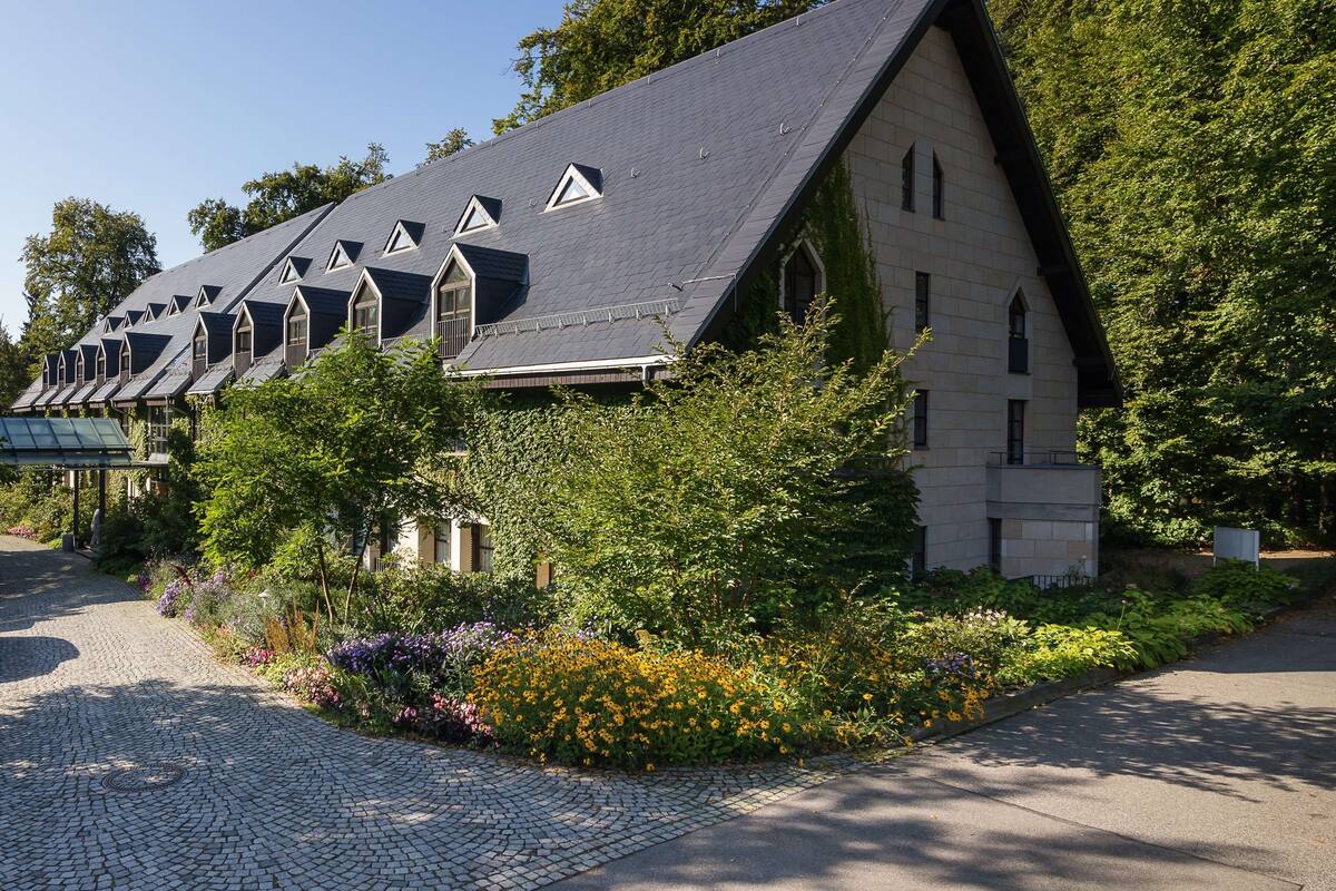 Eine Reihe traditioneller Gebäude mit steilen Satteldächern und Dachgauben, umgeben von üppiger Vegetation und einem Pflasterweg.