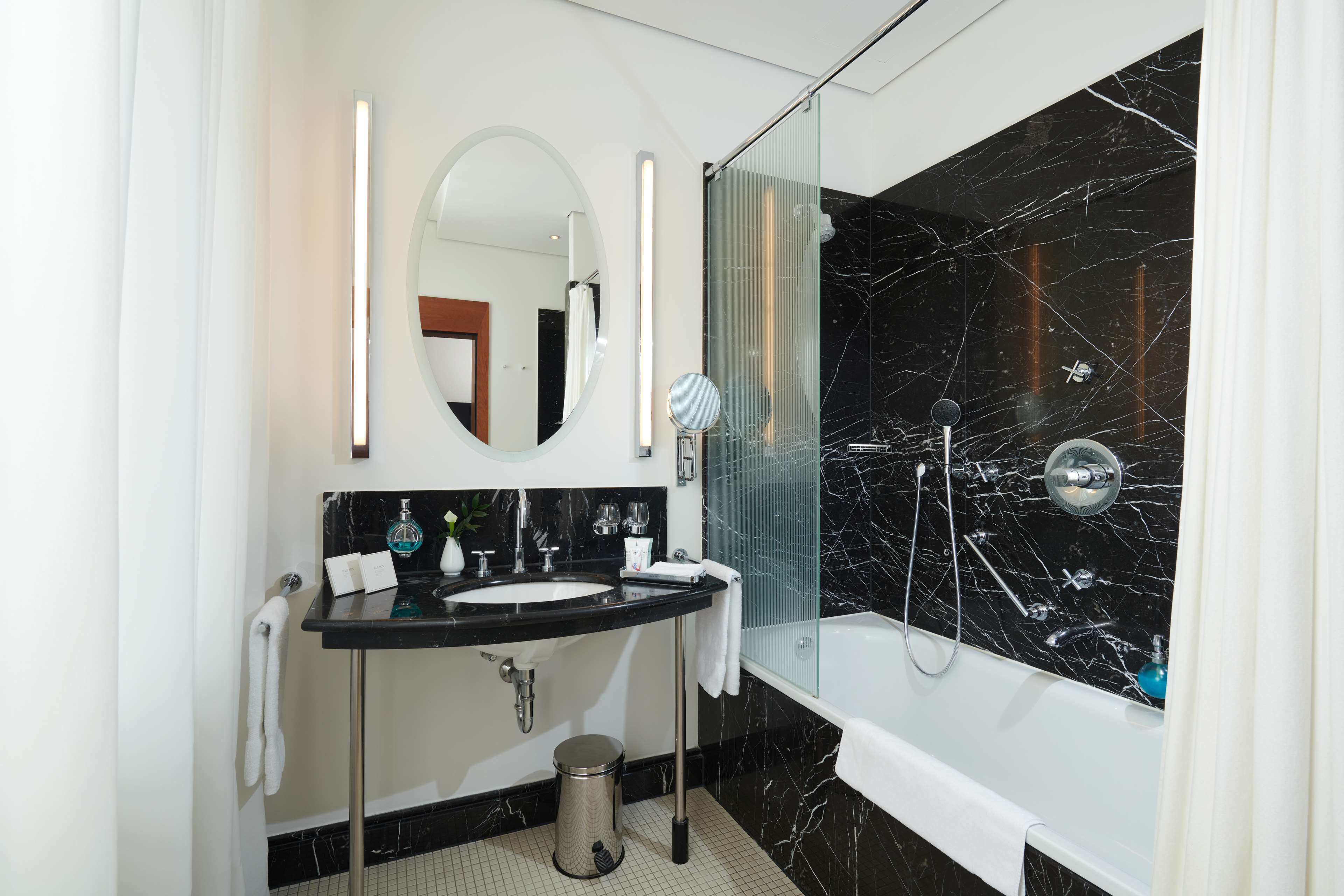 Une salle de bain moderne avec une douche en marbre noir, une baignoire blanche et un lavabo sur un plan de toilette noir.