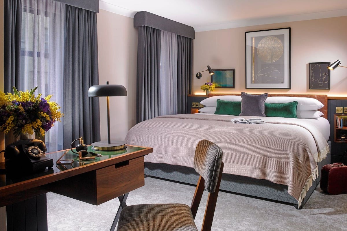 Una habitación de hotel con una cama grande, un escritorio con teléfono, una silla y una lámpara.