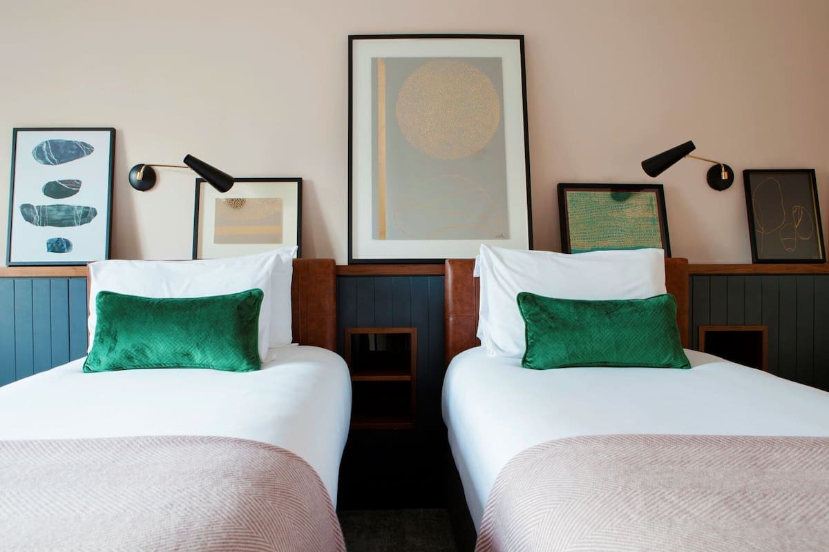 Dos camas individuales con almohadones verdes, un cuadro abstracto enmarcado sobre cada cama y una fotografía de rocas en la pared.
