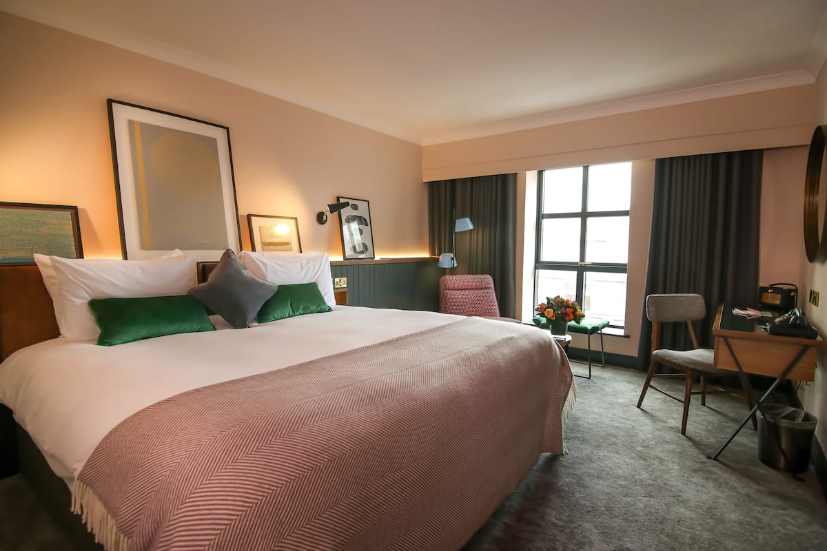 A hotel room with a large bed, a desk, a chair, and a window with curtains.