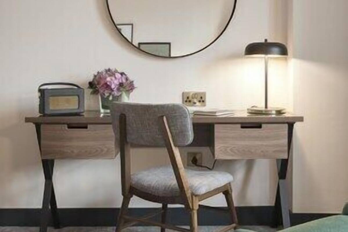 A room with a desk, chair, lamp, and a round mirror on the wall.