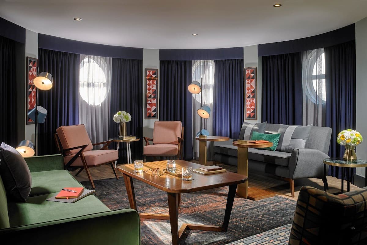 Una sala de estar moderna con un sofá verde, dos sillones, un sofá gris, una mesa de centro de madera y un tapiz estampado.