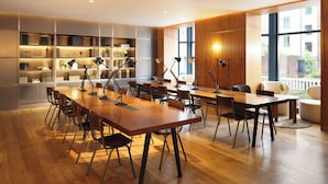 A spacious conference room with a long wooden table, multiple chairs, and standing lamps. Shelves with books and decorative items line the walls. - The Alex (Dublin)
