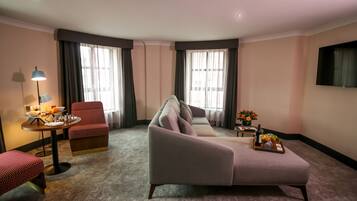 Quarto de hotel com sofá, poltrona e uma mesinha com luminária e bandeja de frutas.