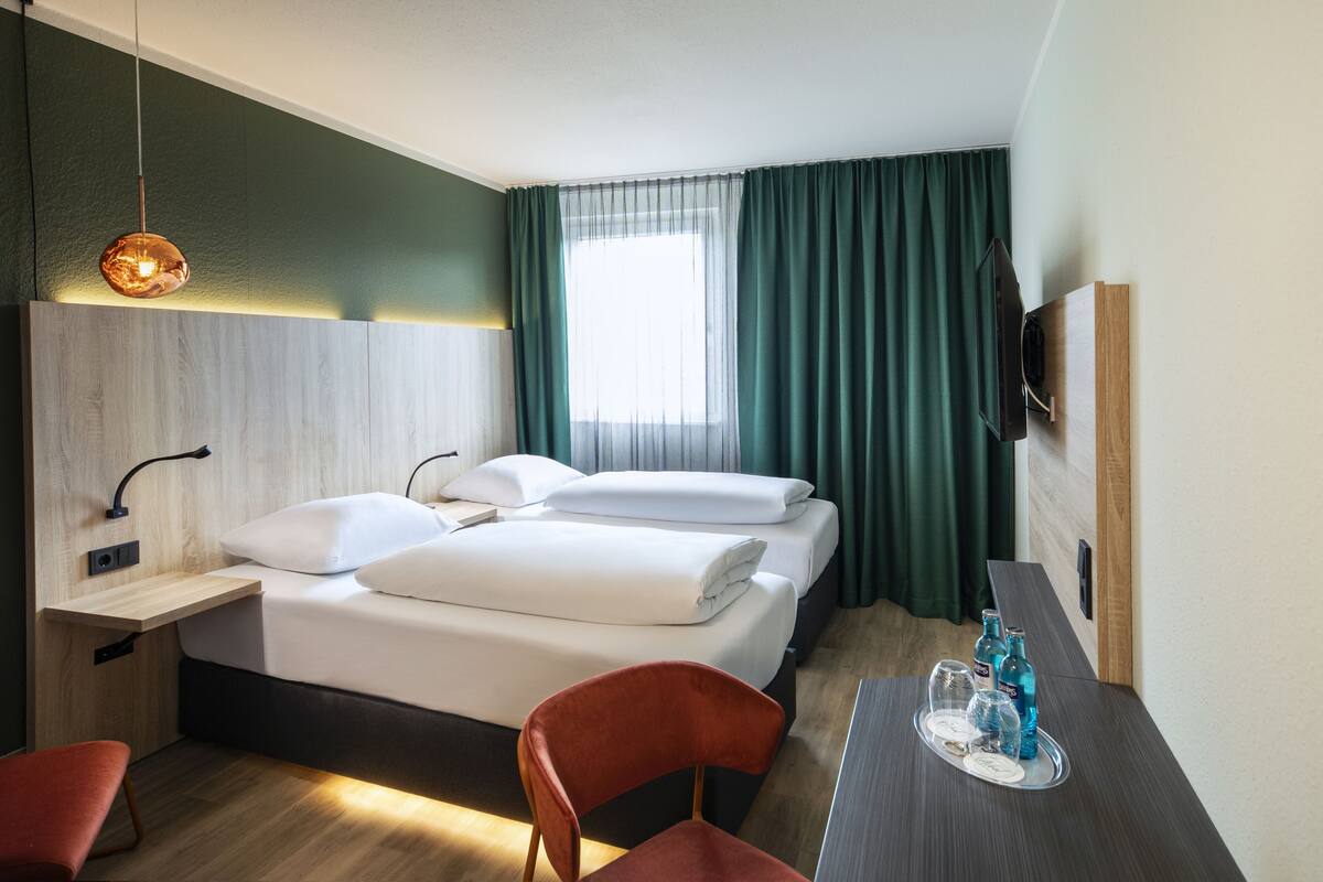 Ein Hotelzimmer mit Bett, Schreibtisch, Stuhl, Fernseher und einem Fenster mit Vorhängen.