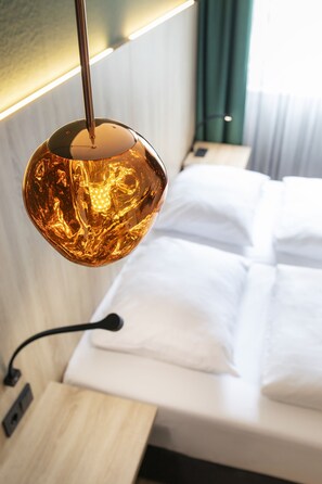 A modern hotel room with a bed, a bedside table, and a unique spherical pendant light.