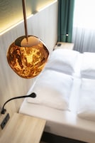 Quarto de hotel moderno com cama, mesa de cabeceira e uma luminária pendente esférica singular.