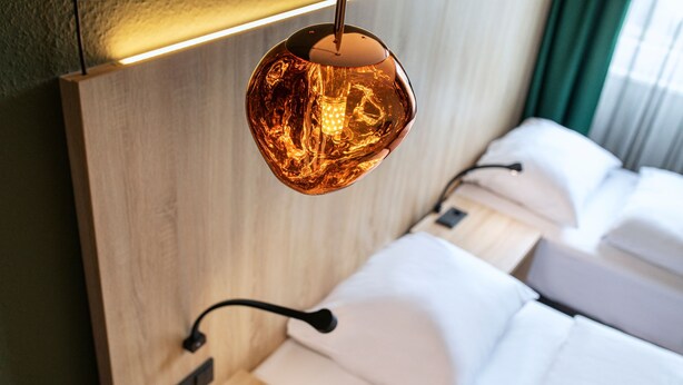A modern hotel room with a wooden headboard, a hanging spherical light fixture, and neatly made beds.
