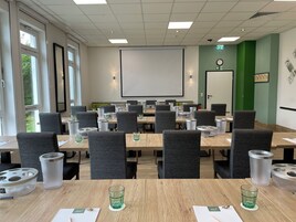 Uma sala de conferências com mesas, cadeiras e uma tela de projeção.