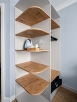 Una moderna mensola curva in legno con diversi scomparti, alcuni contenenti oggetti come un bollitore e bicchieri.